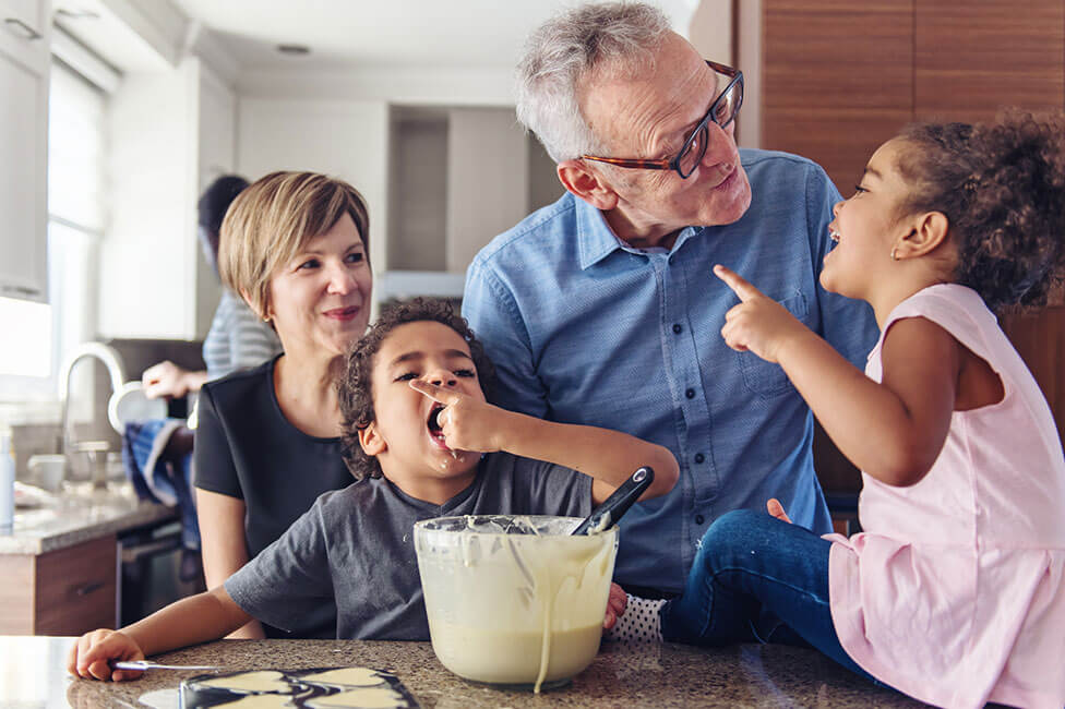 grandpa and grandma baking with little grandkids sitting on the kitchen counter