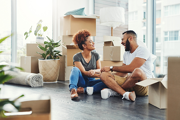 young couple sitting on the floor of their living room amongst all the moving boxes