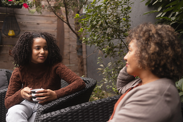 two women sitting on a patio chatting over coffee