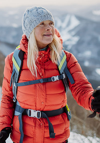 a woman in her 60s wearing a red jacket hiking on a snow capped mountain